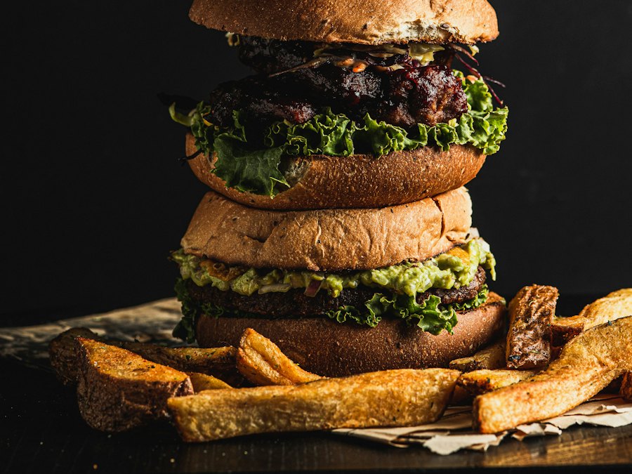 Two stacked gourmet burgers with guacamole and fries