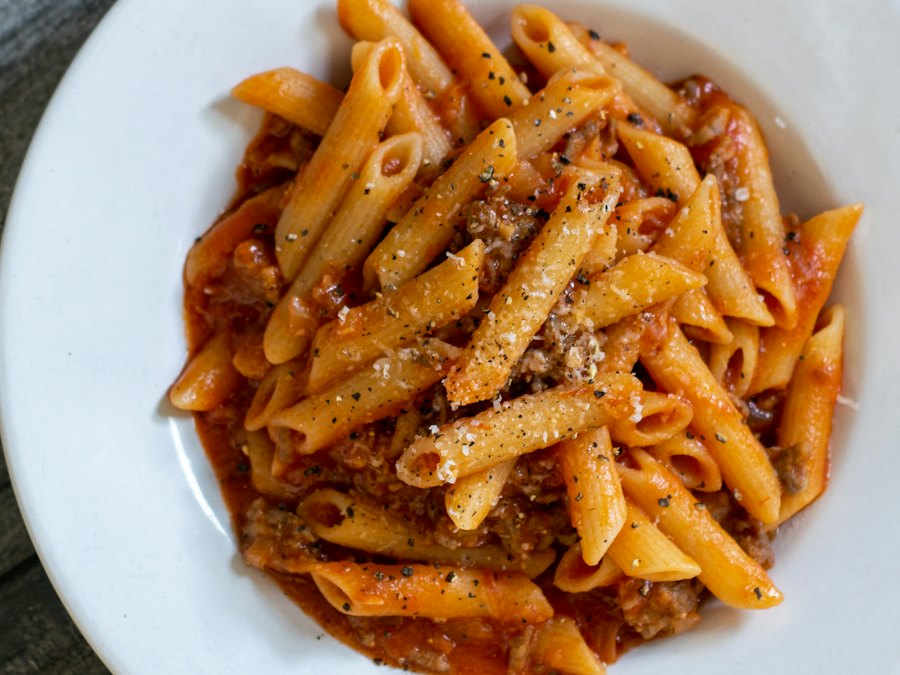 Penne pasta with meat sauce and grated cheese in a white bowl